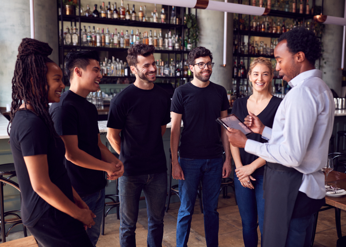A group of restaurant staff gathered for wine training, listening attentively to their manager